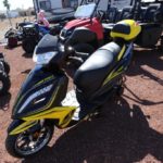 A yellow and black scooter parked on top of a dirt field.