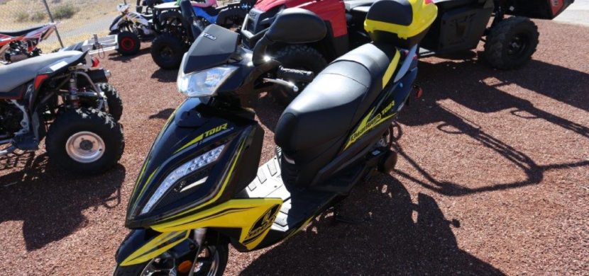 A yellow and black scooter parked on top of a dirt field.