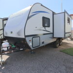 A white and blue trailer parked on top of gravel.