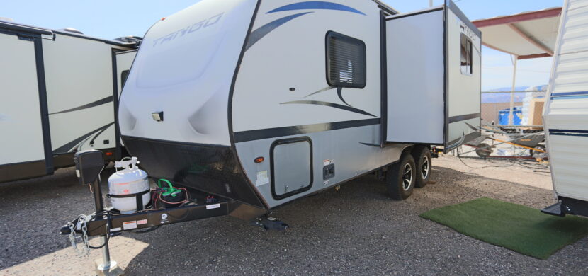 A white and blue trailer parked on top of gravel.