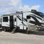 A white and black rv parked on top of a sandy beach.