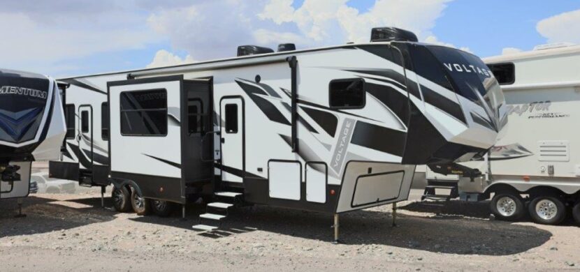 A white and black rv parked on top of a sandy beach.