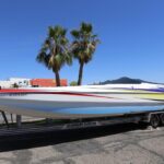 A boat is parked on the trailer in front of palm trees.