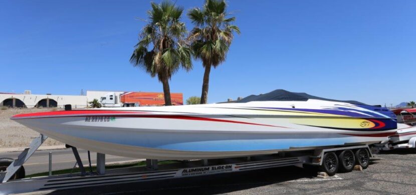 A boat is parked on the trailer in front of palm trees.